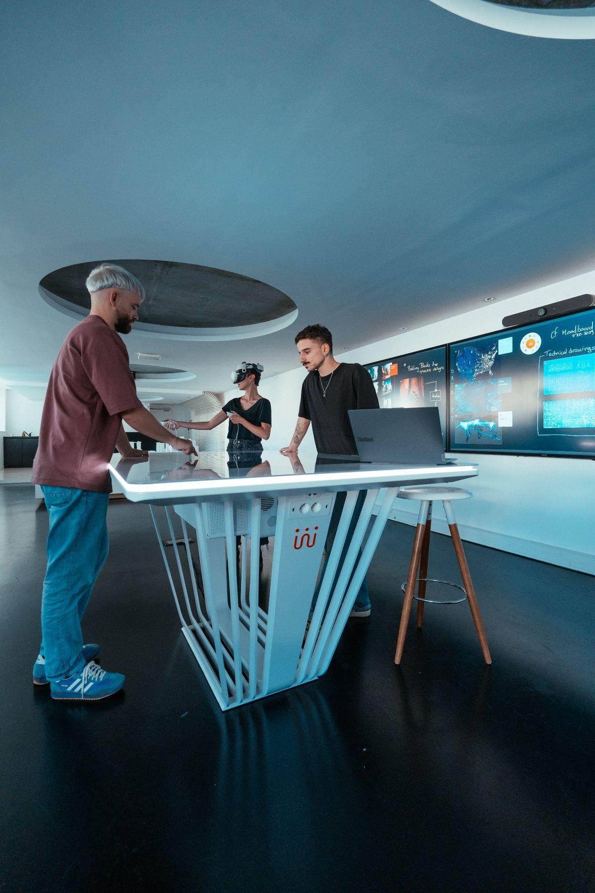 VR and MR design review around a Shariiing touch table, one of the three colleagues wearing a mixed reality headset